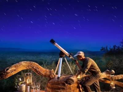 A man using a telescope to stargaze under a clear night sky in Madikwe Game Reserve, South Africa.
