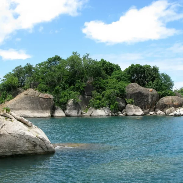 Rocky island surrounded by clear blue waters in Lake Malawi, with lush greenery.